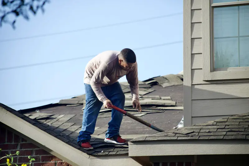 Worker removing damaged shingles from a roof